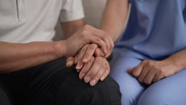 cropped view hand of mature woman patting on resident care attendant’s hand, showing trust in him. the male also taps the female’s hand, giving support concept