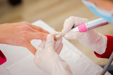 A woman is getting a manicure of nails. Removing the nail plate with a milling machine