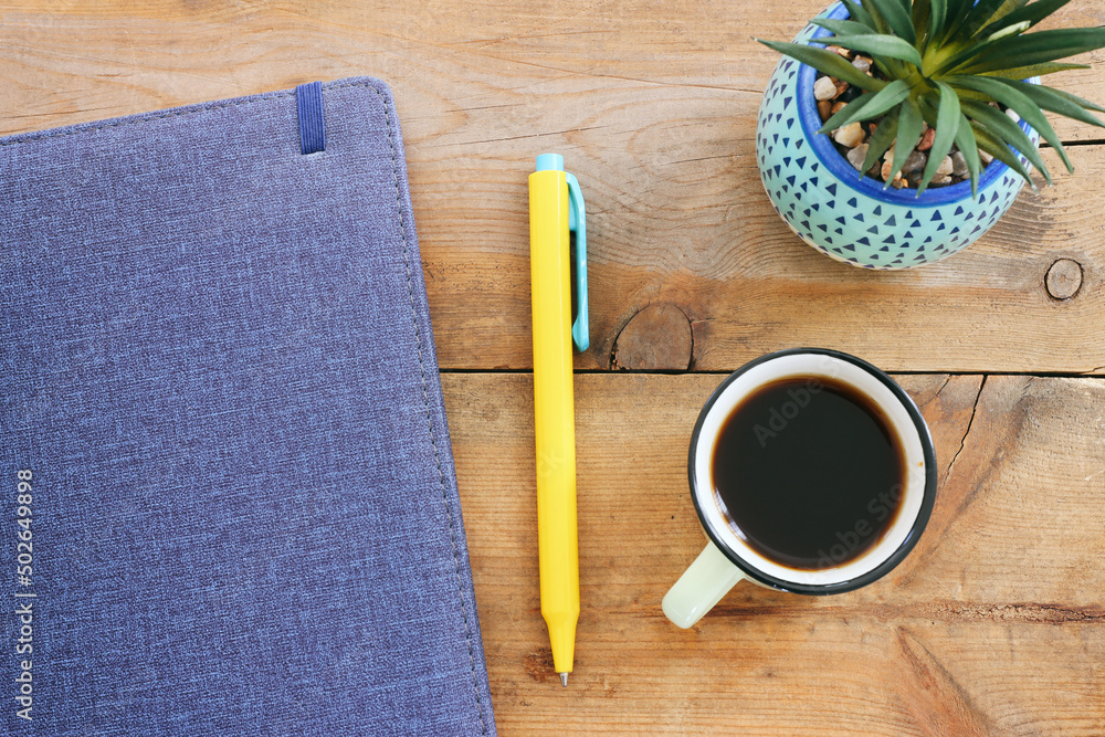 Poster top view image of notebook and cup of coffee over wooden desk. ready for adding text or mockup.