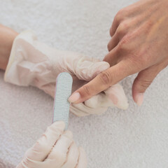 Manicurist uses nail file to nails. A woman is getting a manicure of nails. The beautician files the client's nails