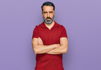 Middle aged man with beard wearing casual red t shirt skeptic and nervous, disapproving expression on face with crossed arms. negative person.