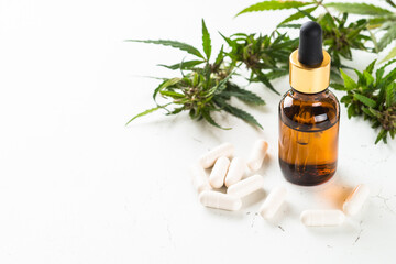 Fototapeta premium CBD pills and CBD oil in glass bottle at white table. Cannabis medicine. Sedative, antibiotic, antioxidant using.