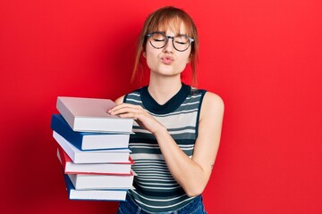 Redhead young woman holding a pile of books looking at the camera blowing a kiss being lovely and sexy. love expression.