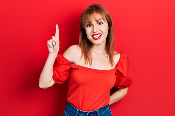 Redhead young woman wearing casual red t shirt pointing finger up with successful idea. exited and happy. number one.