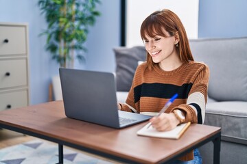 Fototapeta premium Young woman using laptop writing on notebook at home