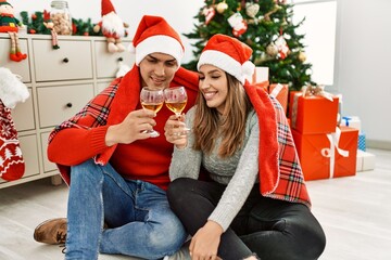 Young couple wearing christmas hat covering with blanket. Sitting on the floor toasting with champagne at home.