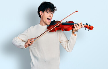 Handsome hipster young man playing violin celebrating crazy and amazed for success with open eyes screaming excited.