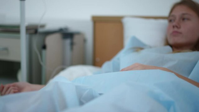 Unrecognizable Female Nurse Holding Hand Of Teenage Patient And Leaving Hospital Ward. Caring Caucasian Young Slim Woman Supporting Endorsing Ill Girl Lying In Bed In Medical Clinic