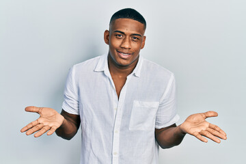 Young black man wearing casual white shirt clueless and confused expression with arms and hands...