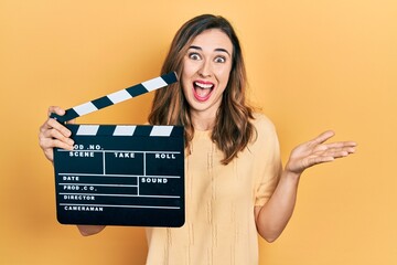 Young hispanic girl holding video film clapboard celebrating achievement with happy smile and...