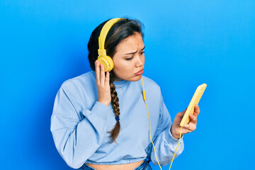 Young hispanic girl using smartphone and headphones depressed and worry for distress, crying angry...