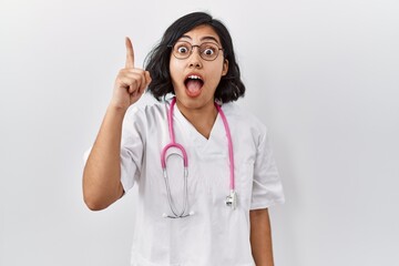 Young hispanic doctor woman wearing stethoscope over isolated background pointing finger up with successful idea. exited and happy. number one.