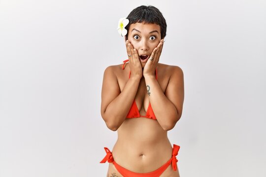Young hispanic woman with short hair wearing bikini afraid and shocked, surprise and amazed expression with hands on face
