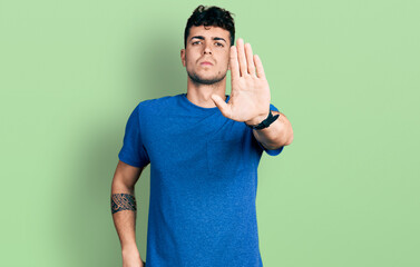 Young hispanic man wearing casual t shirt doing stop sing with palm of the hand. warning expression...