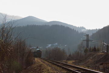 old passenger train runs on the railway track in the light of sunset in early spring between the...
