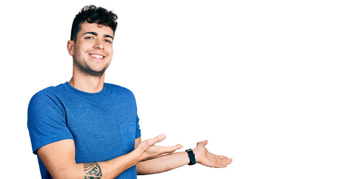 Young hispanic man wearing casual t shirt inviting to enter smiling natural with open hand