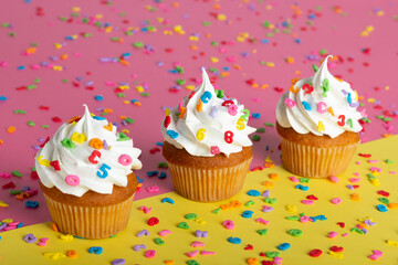 Three decorated cupcakes in a row on a vibrant background, scattered with multicolored confetti.