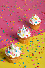 Close-up view of cupcakes adorned with whipped cream and sprinkles, placed on a split-color background.