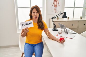 Hispanic woman supporting blood donation in shock face, looking skeptical and sarcastic, surprised...