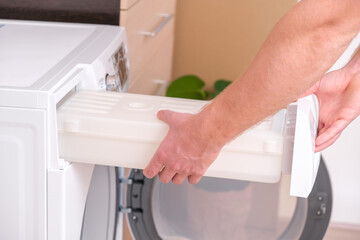 A man takes out a container from the dryer to collect water squeezed out of wet laundry.
