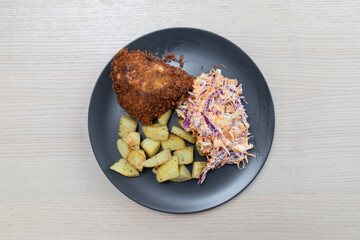 A plate of chicken schnitzel, coleslaw, and fried potato.