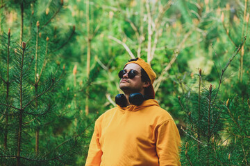 Stylish man in hoodie listen music in headphones in pine tree forest