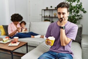 Hispanic father of interracial family drinking a cup coffee looking stressed and nervous with hands on mouth biting nails. anxiety problem.