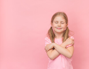 Happy little girl hugging herself on pink background with copy space. I love myself consept.