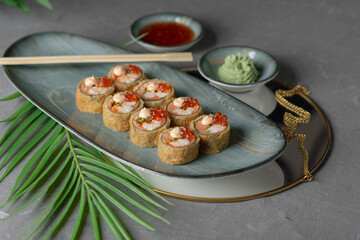 tempura sushi and rolls with red caviar on a black dish and gray background