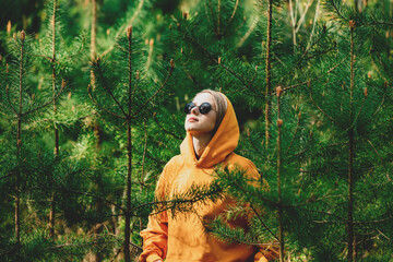 girl in yellow hoodie listening to the birds singing in the pine forest