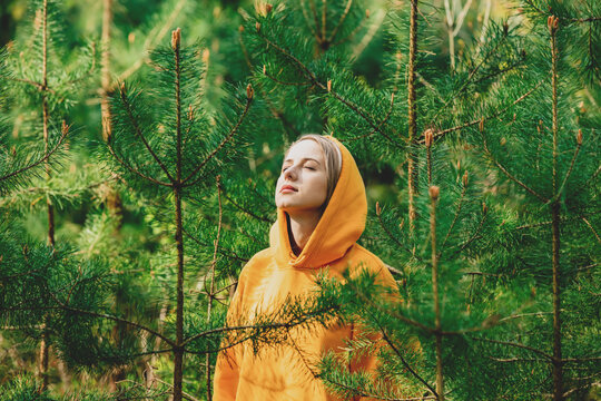 girl in yellow hoodie listening to the birds singing in the pine forest