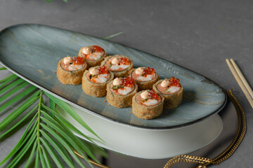 tempura sushi and rolls with red caviar on a black dish and gray background