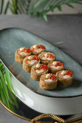 tempura sushi and rolls with red caviar on a black dish and gray background