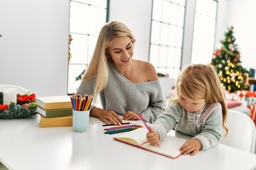 Fototapeta premium Mother and daughter drawing on notebook sitting by christmas tree at home