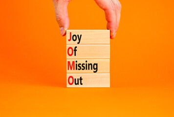 JOMO joy of missing out symbol. Concept words JOMO joy of missing out on wooden blocks on a beautiful orange background. Businessman hand. Business JOMO joy of missing out concept. Copy space.