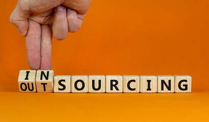 Outsourcing or insourcing symbol. Businessman turns wooden cubes and changes the word Outsourcing to Insourcing. Beautiful orange background. Business outsourcing or insourcing concept. Copy space.