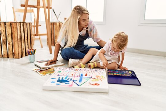 Mother and daughter smiling confident drawing sitting on floor at art studio
