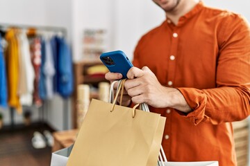 Customer man holding shopping bags and using smartphone at clothing store.