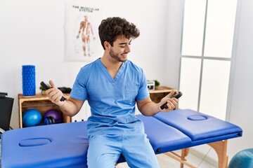 Young hispanic man wearing physio therapist uniform using grip hand at clinic