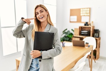 Blonde business woman at the office smiling cheerful showing and pointing with fingers teeth and mouth. dental health concept.