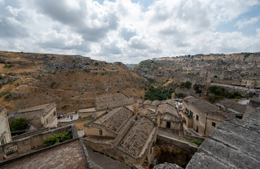 Fototapeta na wymiar Matera, Basilicata, Italy. August 2021. Splendid daytime panoramic view of the stones of Matera. On the hill on the left the ancient caves are recognizable. On the right the old dark stone houses.