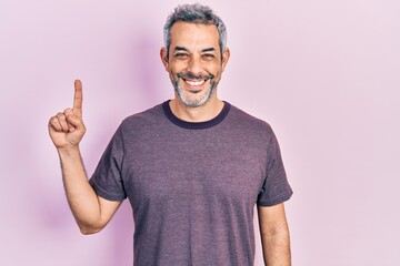 Fototapeta premium Handsome middle age man with grey hair pointing with index finger smiling with a happy and cool smile on face. showing teeth.