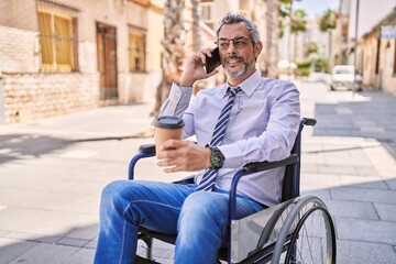 Middle age hispanic man sitting on wheelchair talking on the smartphone at street