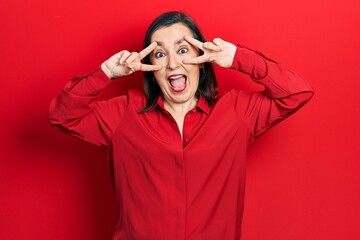 Middle age hispanic woman wearing casual clothes doing peace symbol with fingers over face, smiling cheerful showing victory