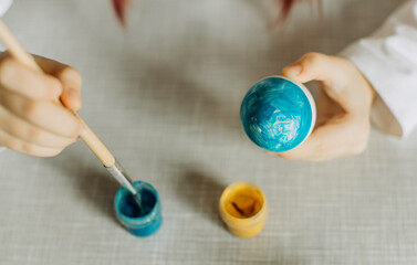 Ukrainian girl paints the egg blue and yellow. The child loves and supports his country. Cute little child girl painting with blue and yellow colors Easter eggs. Hands of a girl with a easter egg. Top