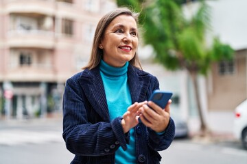 Fototapeta premium Middle age woman business executive using smartphone at street