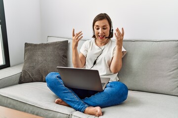 Middle age hispanic woman sitting on the sofa wearing headset at home