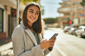 Young hispanic girl smiling happy using smartphone at the city.