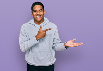 Young handsome hispanic man wearing casual sweatshirt amazed and smiling to the camera while presenting with hand and pointing with finger.