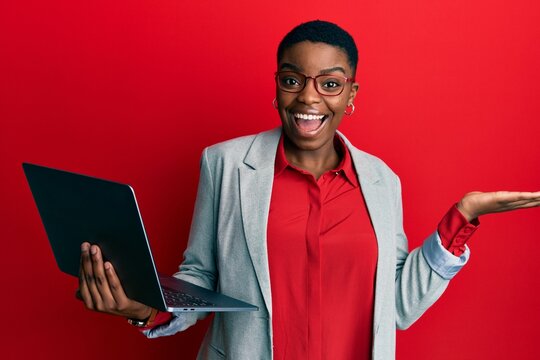 Young african american woman holding laptop celebrating achievement with happy smile and winner expression with raised hand